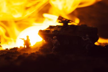 Toy soldiers with tank, fire and sunset on black background, battle scene clipart