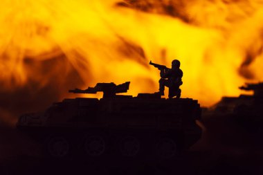 Battle scene with silhouettes of toy warrior and tanks with fire at background clipart