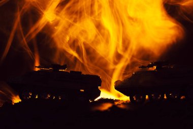 Oyuncak tanklarla savaş sahnesi ve siyah arka planda yangın