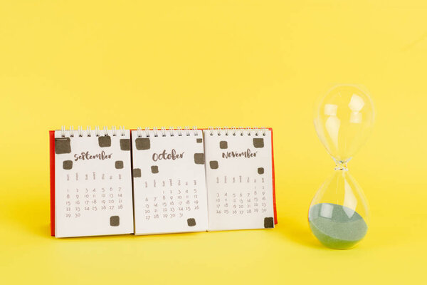 Календарь с осенними месяцами и песочными часами на желтом фоне
