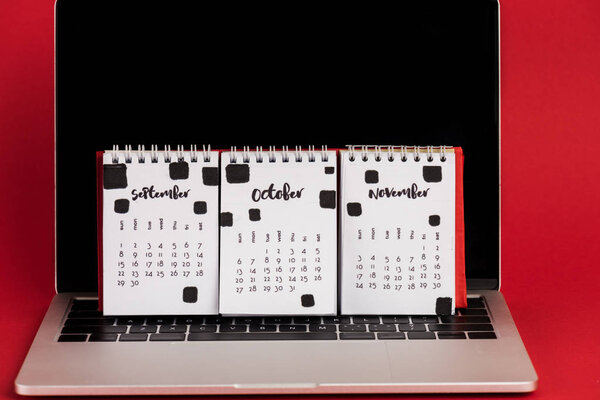 Календарь с осенних месяцев на ноутбуке с пустым экраном на красном фоне
