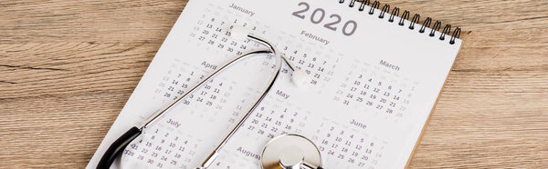 Panoramic shot of stethoscope on calendar of 2020 year on wooden background