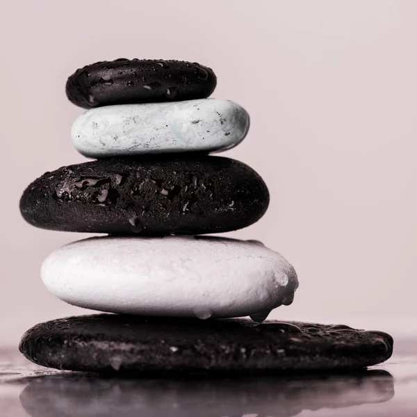 Su damlalarıyla doldurulmuş makro Zen taşları pembe bardakta izole edilmiş ıslak bardakta. 