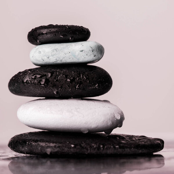 Macro shot of stacked zen stones in water drops on wet glass isolated on pink 