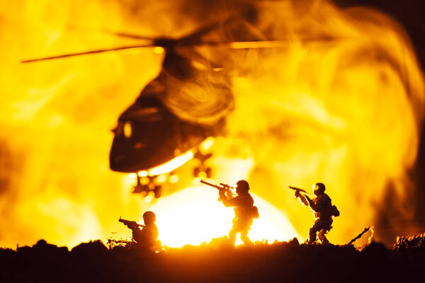 Battle scene with toy warriors and helicopter in smoke with sunset at background