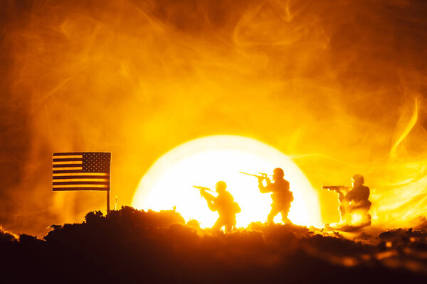 Battle scene of toy soldiers, american flag and fire with sunset at background