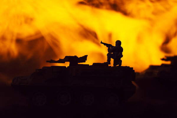 Battle scene with silhouettes of toy warrior and tanks with fire at background
