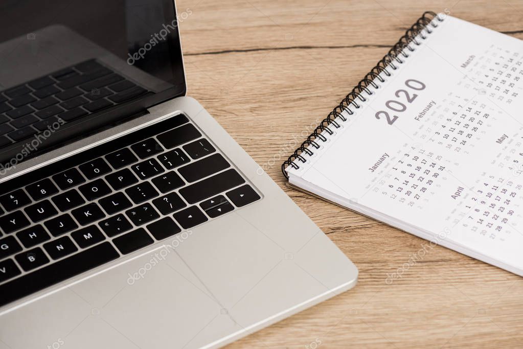 Laptop with blank screen and calendar of 2020 year on wooden background