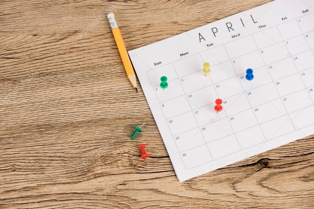 High angle view of pencil, office pins and calendar of april on wooden background