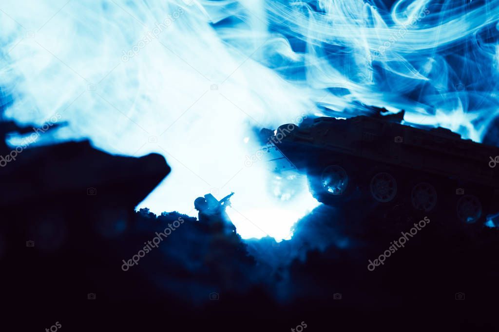 Toy tanks and soldier with blue smoke on black background, battle scene