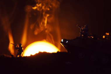 Oyuncak savaşçılarla savaş sahnesi ve arka planda günbatımı ile duman içinde tank
