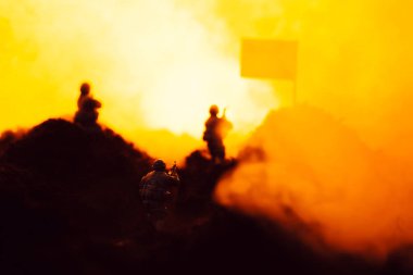 Selective focus of toy warriors on battleground with smoke, flag and fire at background clipart