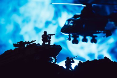 Scene of battle with toy warriors, tank and helicopter with smoke on blue background clipart