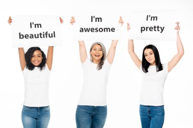 happy multicultural women holding posters with lettering above head isolated on white  clipart
