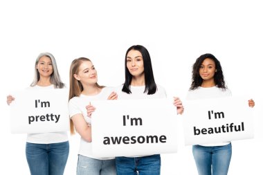 happy multicultural women in denim jeans holding posters with lettering isolated on white  clipart