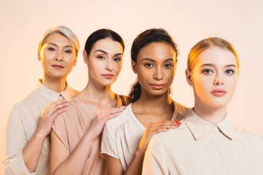 four beautiful multicultural women looking at camera isolated on beige  clipart