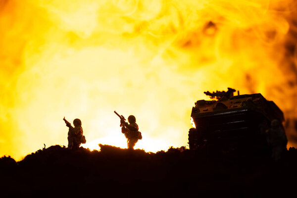 Battle scene with silhouettes of toy tank and soldiers with fire at background