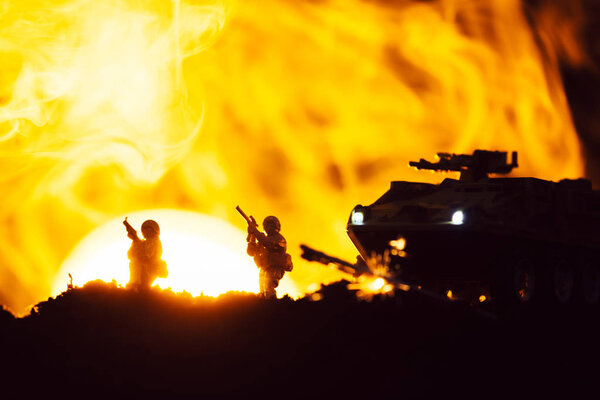 Scene of battle with toy warriors, tank and smoke with sunset at background