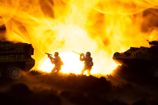 Silhouettes of toy warriors with tanks in fire and sunset at background, battle scene