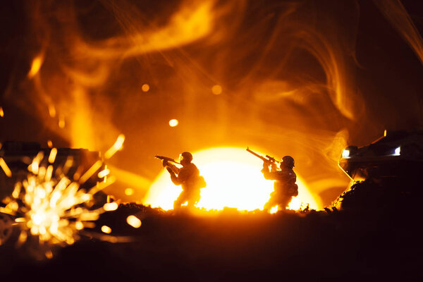Selective focus of toy warriors with tanks near explosion and smoke with sunset at background