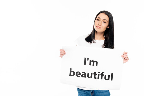 attractive woman looking at camera while holding poster with i`m beautiful lettering isolated on white 