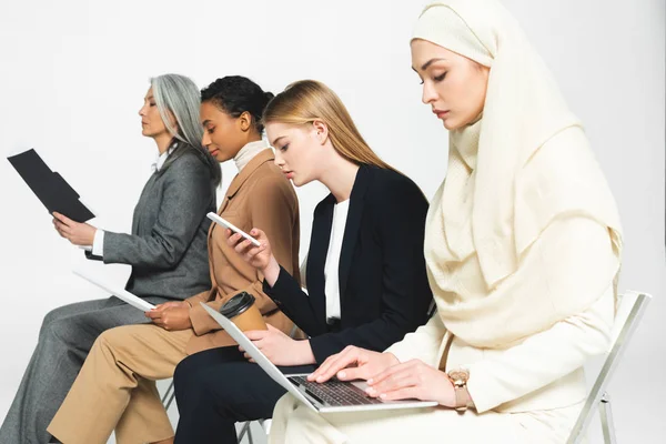 Zijaanzicht Van Multiculturele Zakenvrouwen Zittend Stoelen Met Gadgets Geïsoleerd Wit — Stockfoto
