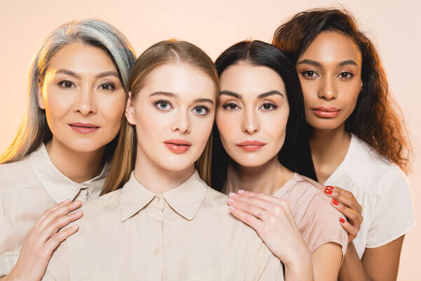 beautiful multicultural women looking at camera isolated on beige 