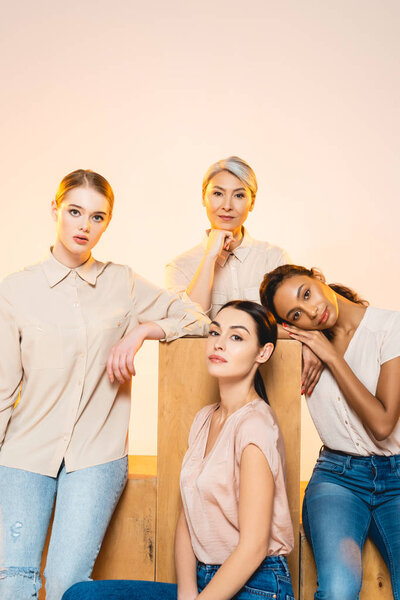 four beautiful multicultural women with makeup looking at camera isolated on beige 