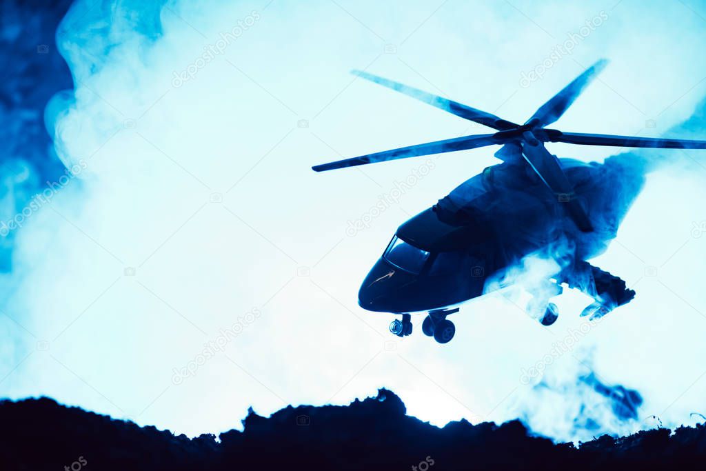 Battle scene with toy helicopter above battleground with smoke on blue background 