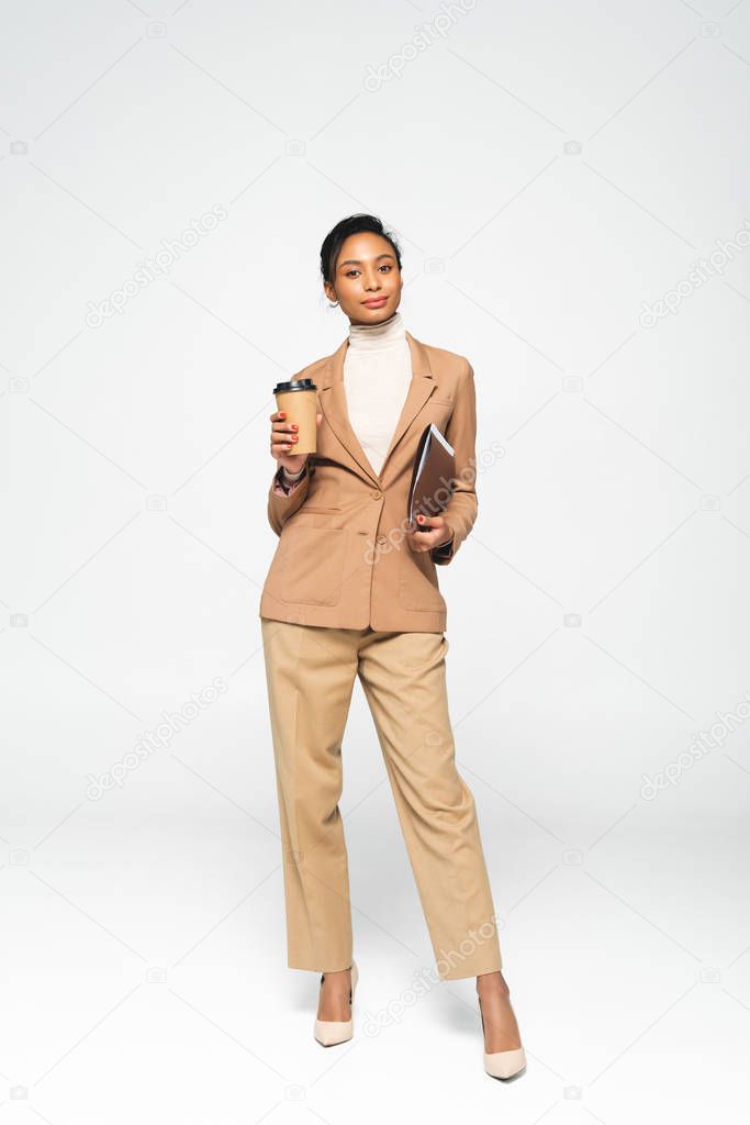 attractive african american businesswoman holding folder and paper cup on white 