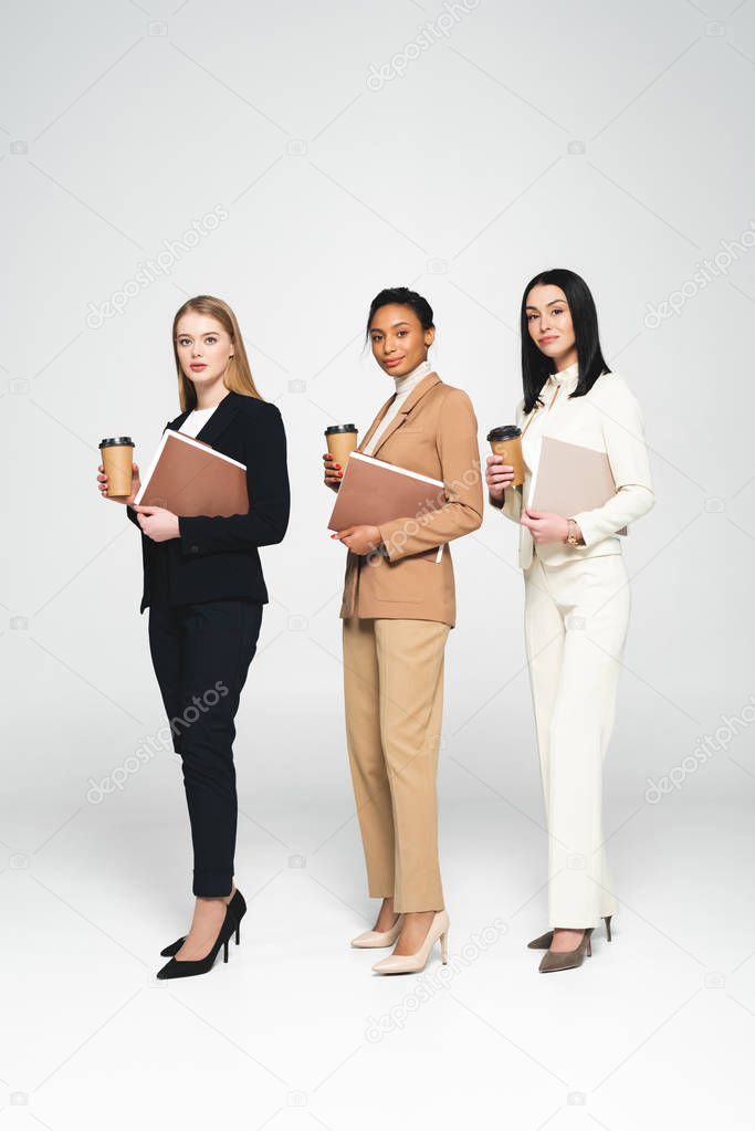 multicultural businesswomen holding disposable cups and folders on white 