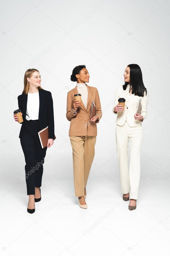 multicultural businesswomen holding paper cups and folders on white 