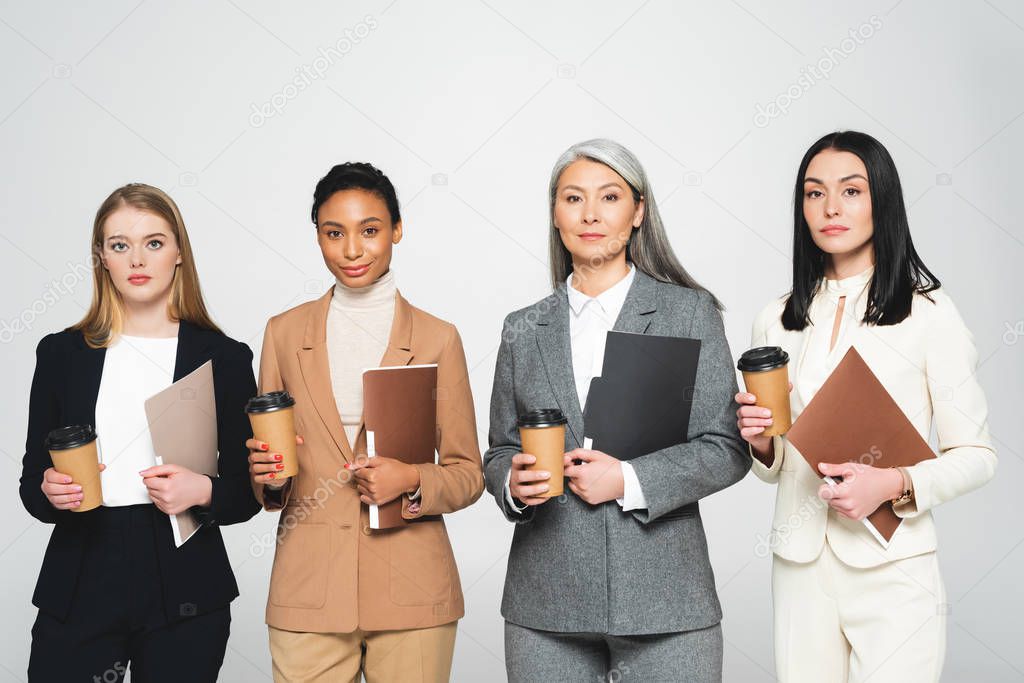 four multicultural businesswomen holding folders and paper cups isolated on white 