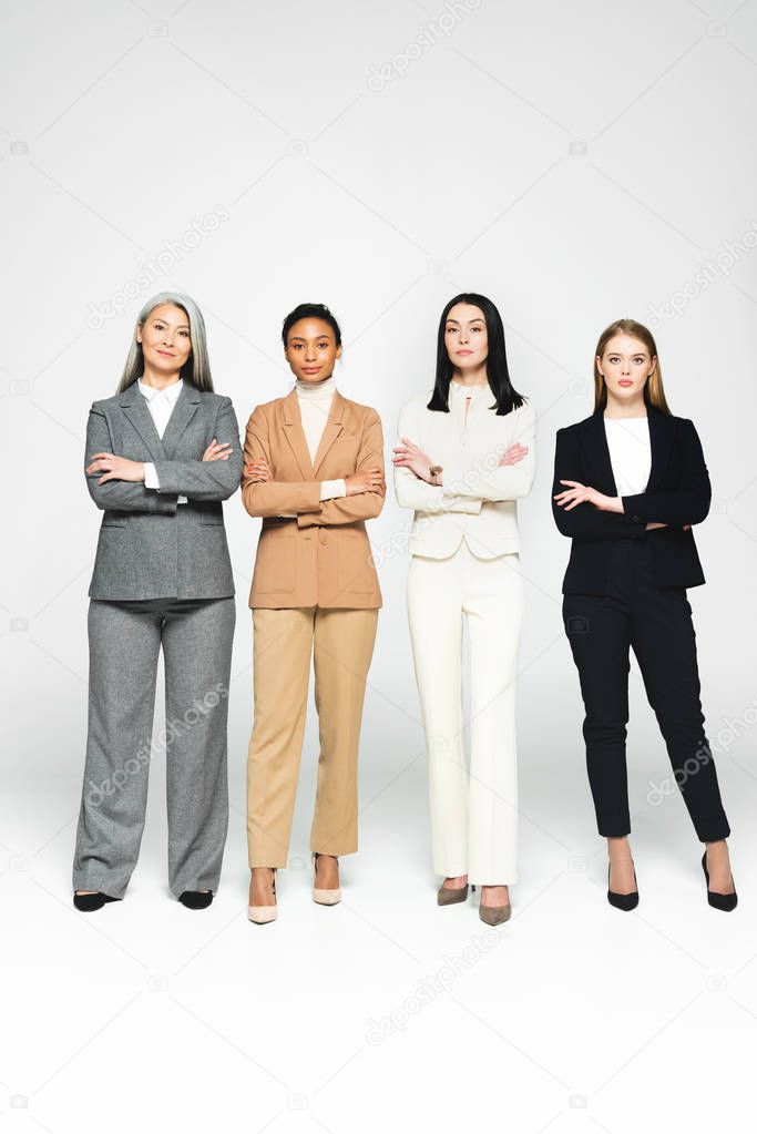 multicultural businesswomen in suits standing with crossed arms on white 