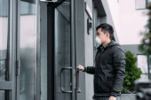 fiatal ázsiai férfi légzőmaszk nyitó ajtó és belépő épület