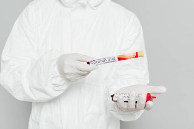 Epidemiyoloji uzmanı tehlikeli madde giysisi içinde kan örneklerini gri renge izole edip test tüpleri tutuyor.