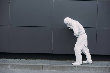 asian epidemiologist in hazmat suit leaning on wall while suffering from symptomatic abdominal pain