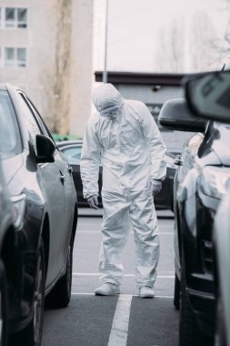 selective focus of asian epidemiologist in hazmat suit and respirator mask inspecting vehicles on parking lot