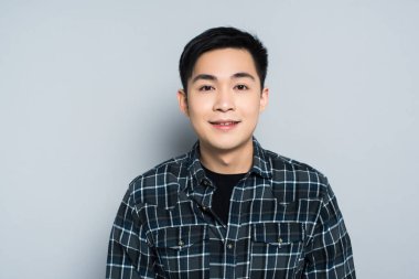 young asian man looking at camera and smiling on grey background