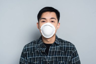 young asian man in respirator mask looking at camera on grey background
