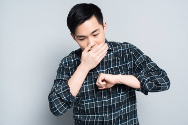 young asian man covering mouth while coughing on grey background clipart