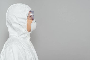 side view of asian epidemiologist in hazmat suit and respirator mask isolated on grey