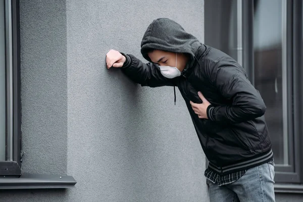 Jovem Homem Máscara Respirador Inclinando Parede Tocando Peito Enquanto Sofre — Fotografia de Stock Grátis