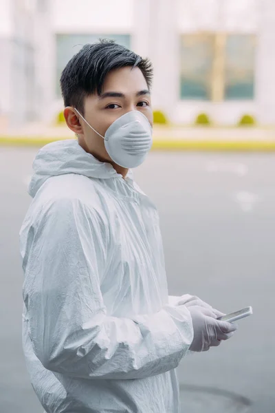 Asian Epidemiologist Hazmat Suit Respirator Mask Holding Smartphone Looking Camera — Free Stock Photo