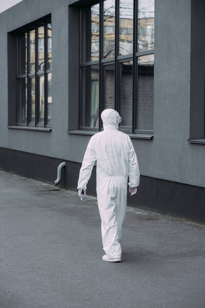 вид на эпидемиолога в защитном костюме, идущего вдоль здания
