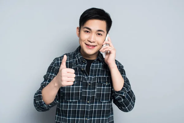 Young Asian Man Smiling Camera While Talking Smartphone Showing Thumb — Stockfoto