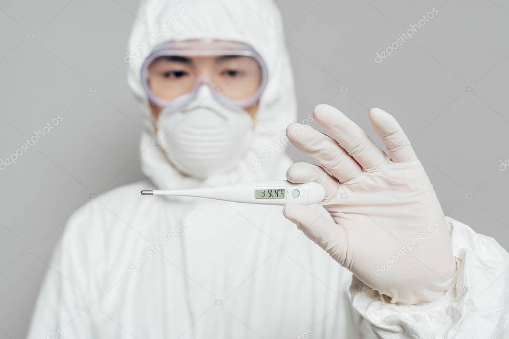 selective focus of asian epidemiologist holding thermometer showing high temperature isolated on grey, panoramic shot