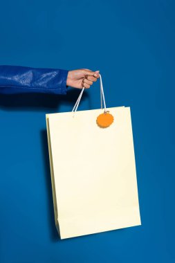cropped view of african american woman holding shopping bag with blank label on blue