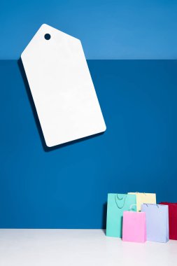 colorful shopping bags and big blank price tag on blue background