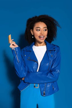 happy african american woman with credit card on blue background